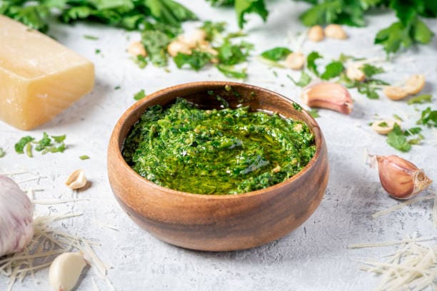 Pistachio pesto in a wooden bowl, surrounded by garlic, cheese, and herbs, ideal for healthy recipes.