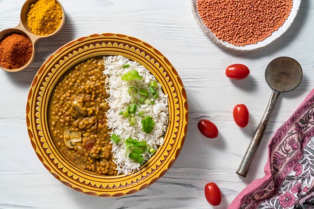 Delicious lentil dal served with colorful veggie rice, garnished with fresh green onions, on a decor.