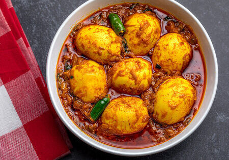 Delicious Indian egg curry with boiled eggs in spicy tomato sauce, garnished with green chilies.