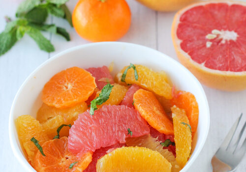 Colorful citrus salad with grapefruit, orange, and mint leaves in a white bowl.