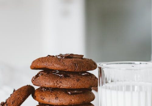 Delicious chewy chocolate tahini cookies stacked with a glass of milk on a light background.