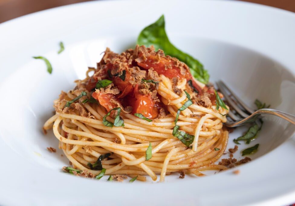 Delicious spaghetti puttanesca with tomatoes, olives, and herbs on a white plate.
