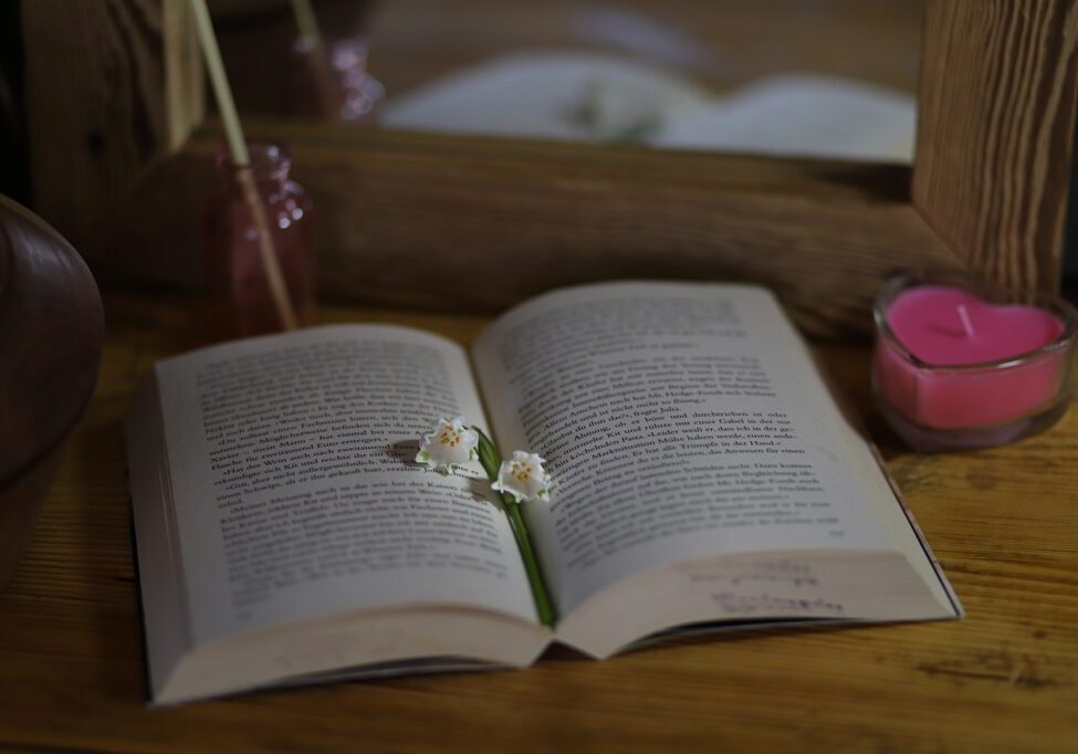Open book with flowers and candle on wooden table for a calming bedtime routine.