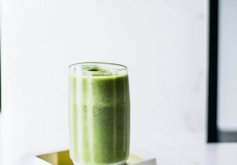 Green MCT-powered matcha smoothie in a glass on a white surface.