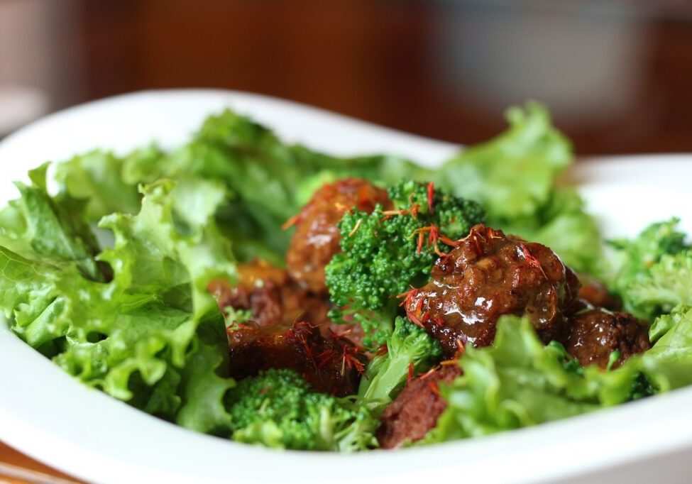Prebiotic gut healthy meatballs with fresh greens and broccoli in a white dish.