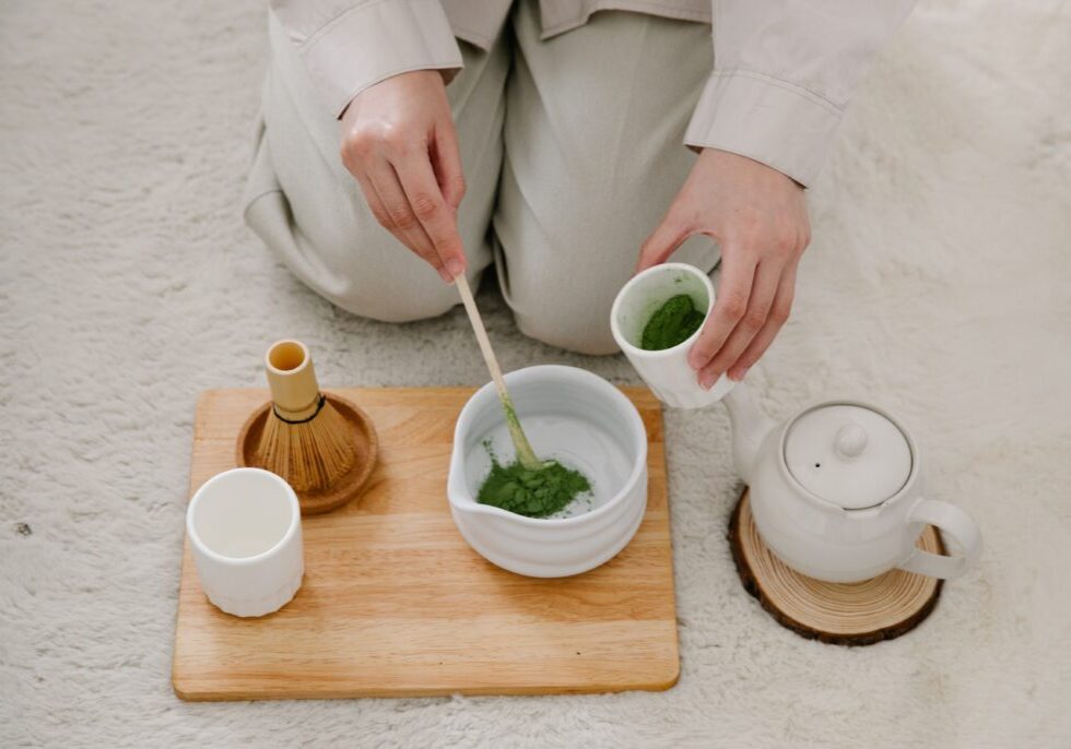 Person preparing fiber powder drink for gut health with tea set and wooden tray.