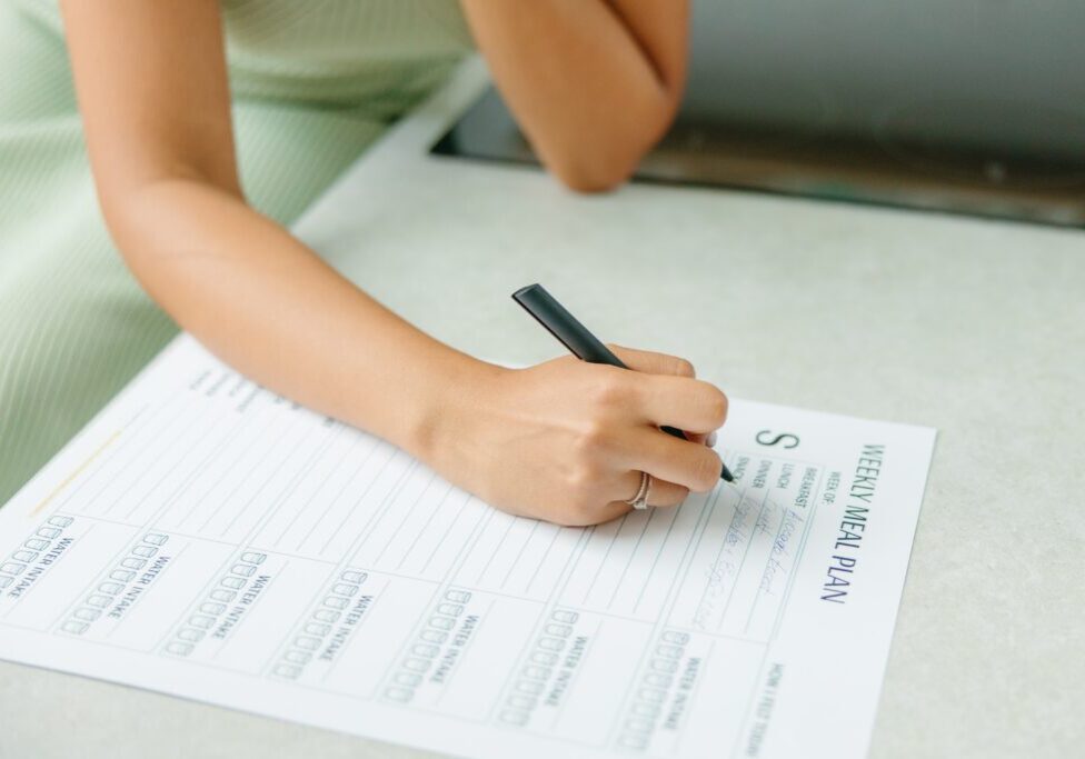 Woman planning meals with a weekly food journal for balanced eating habits.
