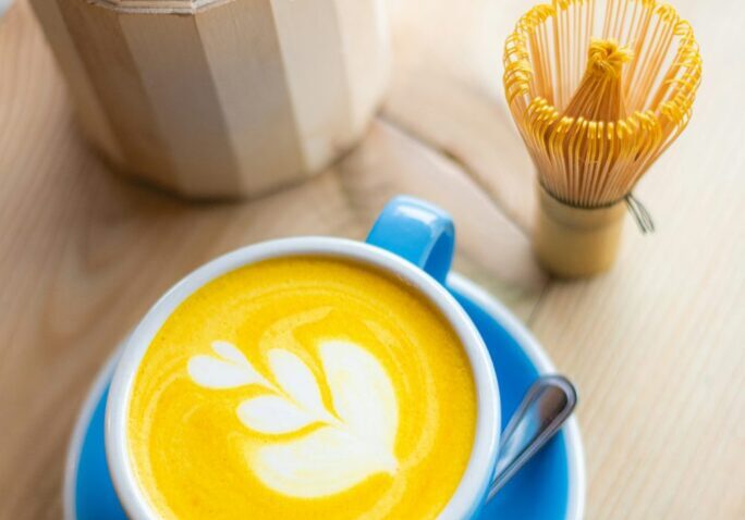 Bright yellow turmeric latte in a blue cup with latte art, on a wooden table.