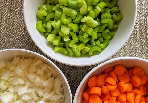 Fresh chopped celery, onions, and carrots in bowls for meal preparation.