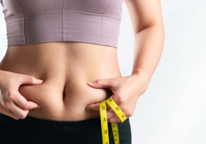woman pinching belly fat while holding tape measure
